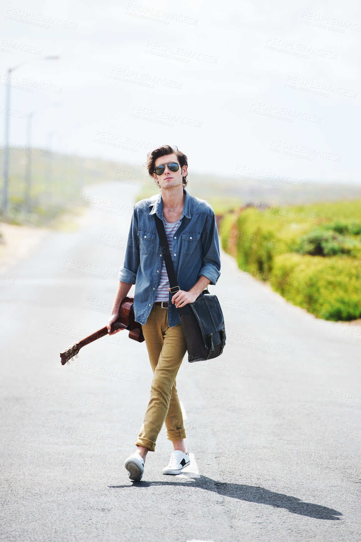 Buy stock photo Trendy young male wearing sunglasses standing in the middle of the road holding a guitar