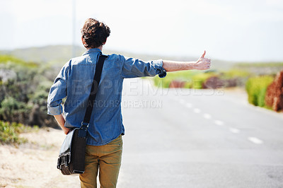 Buy stock photo Rear-view of a young man hitchhiking on the side of the road