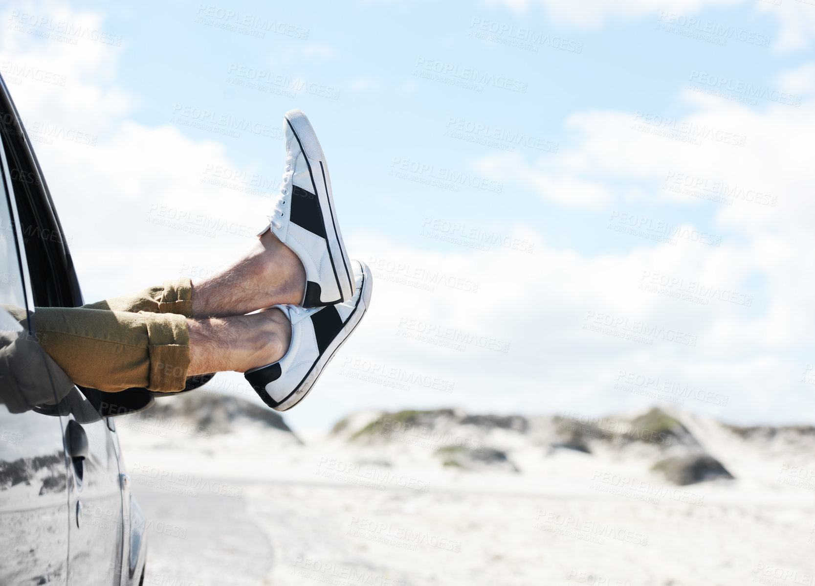 Buy stock photo Two feet wearing sneakers sticking out of a parked car window with dunes in the background