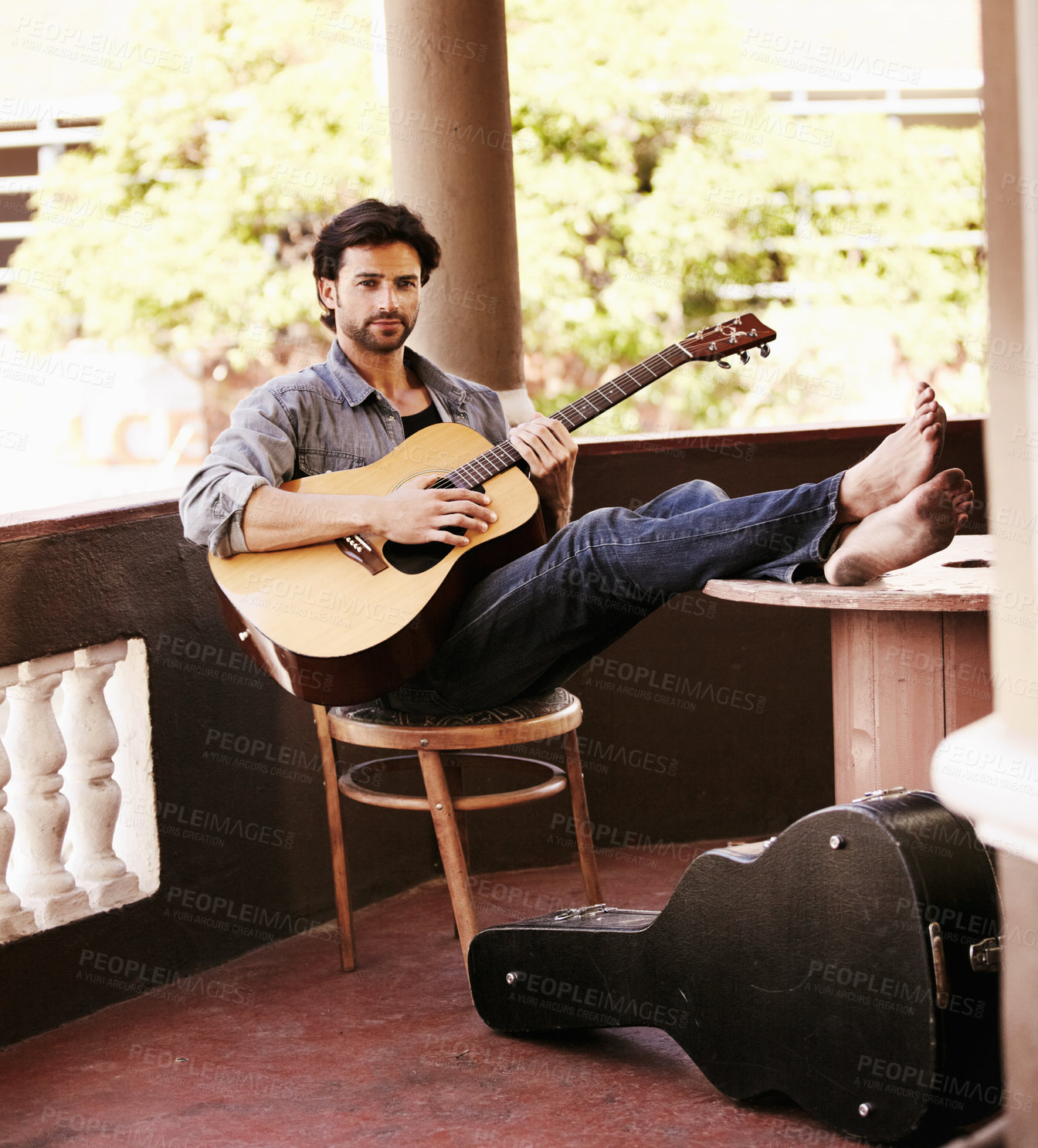 Buy stock photo Handsome young man sitting and playing the guitar while on the verandah