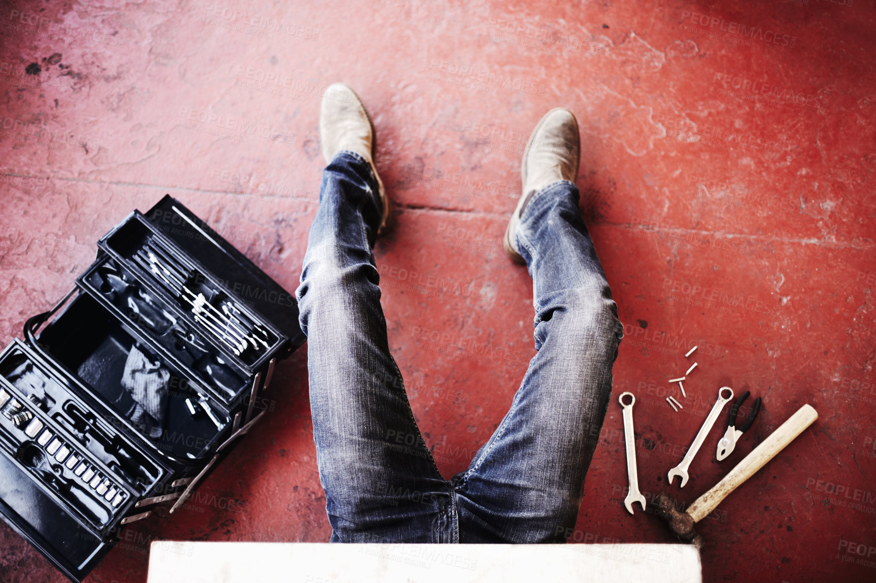 Buy stock photo Closeup of a male mechanic working with equipment and tools lying around and a toolbox with his legs showing while fixing a mechanical part. Handyman making some repairs in a garage or workshop
