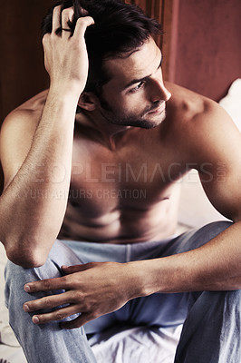 Buy stock photo Sexy young man sitting on the edge of his bed deep in thought
