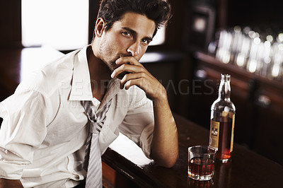 Buy stock photo A handsome young man winding down after work with a drink at the bar