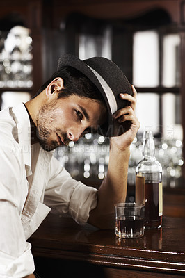 Buy stock photo Portrait, whisky and a man sitting at the bar drinking alcohol in a glass while alone or feeling unhappy. Brandy, drink and beverage with a handsome young male pub customer at a wooden counter