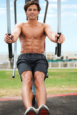 Buy stock photo Smiling and handsome young man working out using outdoor exercise equipment
