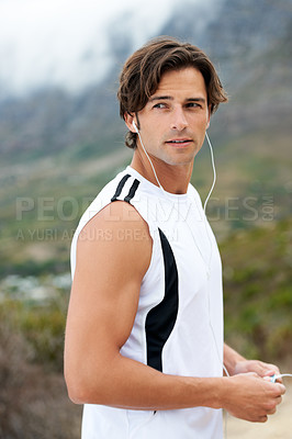 Buy stock photo A handsome young man looking over his shoulder holding an mp3 player and listening to music outside - copyspace