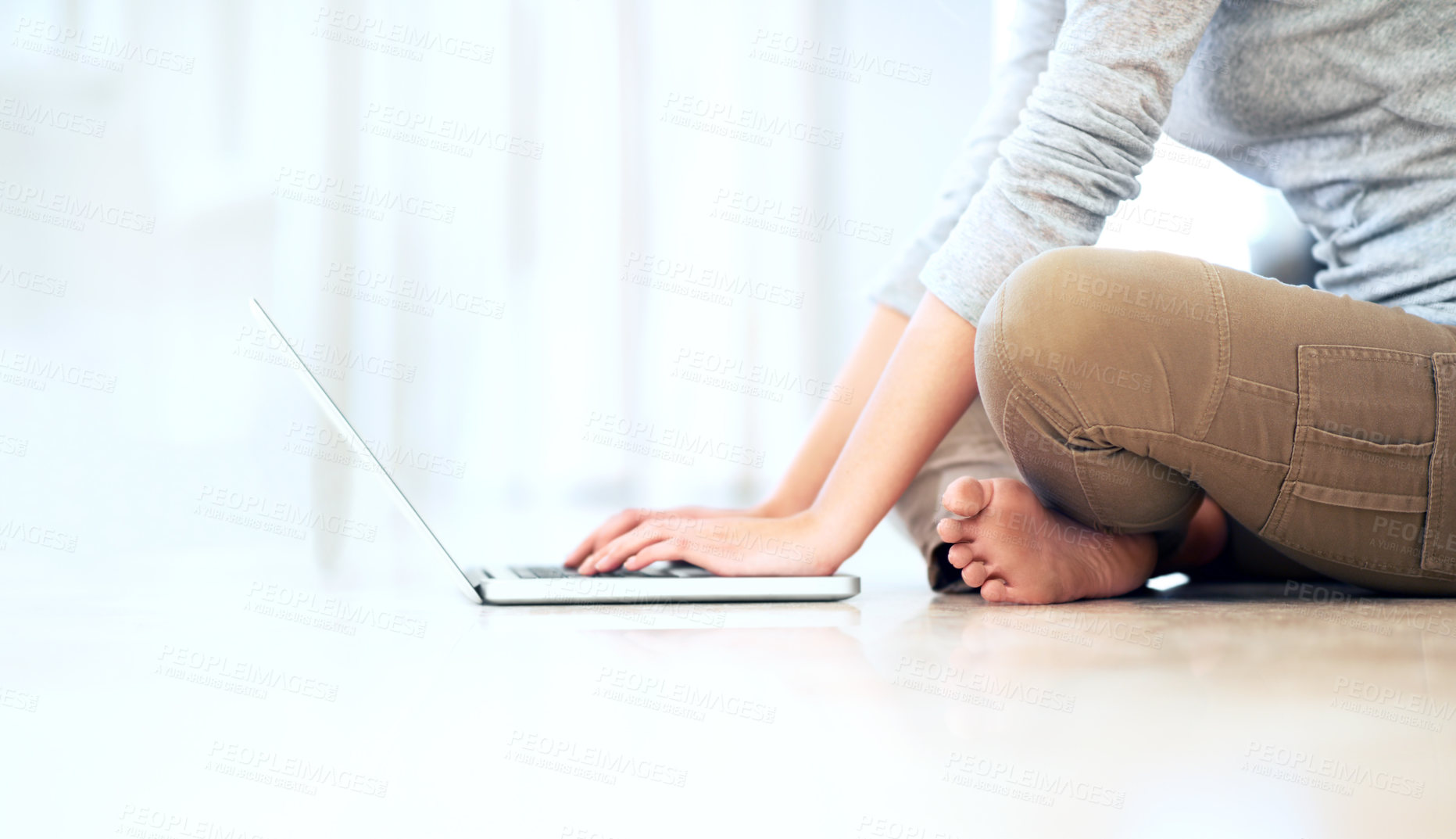 Buy stock photo Cropped image of a young woman sitting on the floor and browsing her laptop