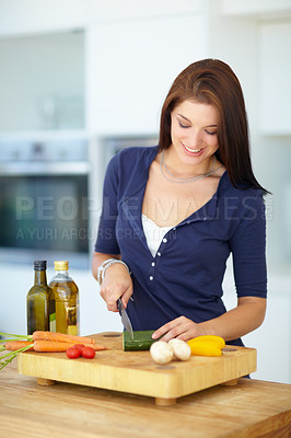 Buy stock photo A pretty young woman chopping some healthy vegetables in her kitchen