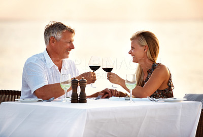Buy stock photo Beach, dinner and couple with sunset, cheers and romance with anniversary, marriage and seaside holiday. Travelling, romantic meal and man with woman, ocean and bonding together with tropical island