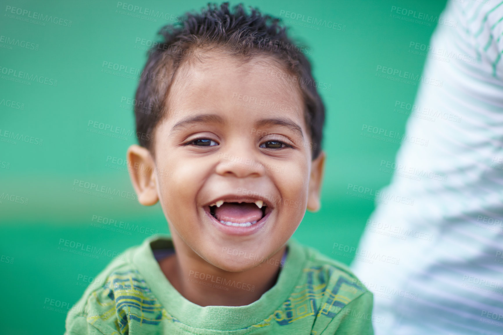 Buy stock photo Portrait of funny little mixed race preschooler with four missing front teeth laughing while sitting against a green background. Adorable little boy showing his gap while looking at the camera