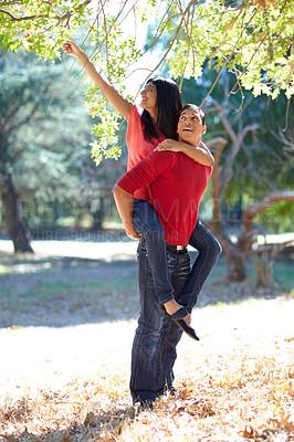 Buy stock photo Shot of a handsome young man giving his girlfriend a piggyback ride in the park