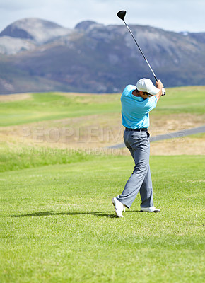 Buy stock photo A young, fit male golfer following through after driving his ball down the fairway