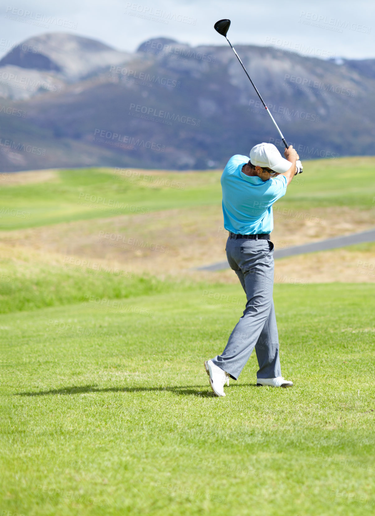 Buy stock photo A young, fit male golfer following through after driving his ball down the fairway