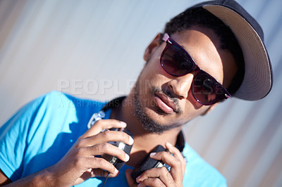 Buy stock photo Portrait, fashion and music with a man in sunglasses outdoor on a blurred background for audio streaming. Face, headphones and hip hop with a confident young person in street wear for urban style