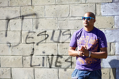 Buy stock photo Shot of a young man standing in front of a wall with graffiti on it