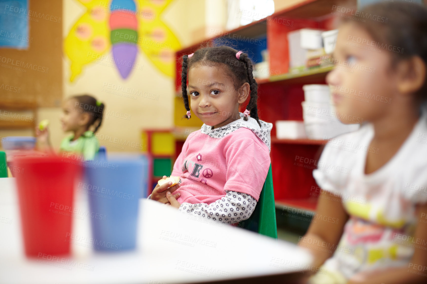 Buy stock photo Child, classroom and lunch in portrait with smile for education at a table with children. Break, kids and learning at school with apple in kindergarten with chair or desk with food with friends.