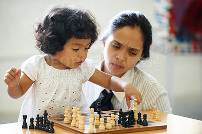 Buy stock photo A cute little girl playing chess while her mom looks on