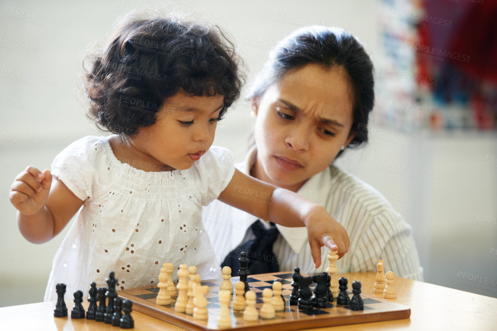 Buy stock photo A cute little girl playing chess while her mom looks on