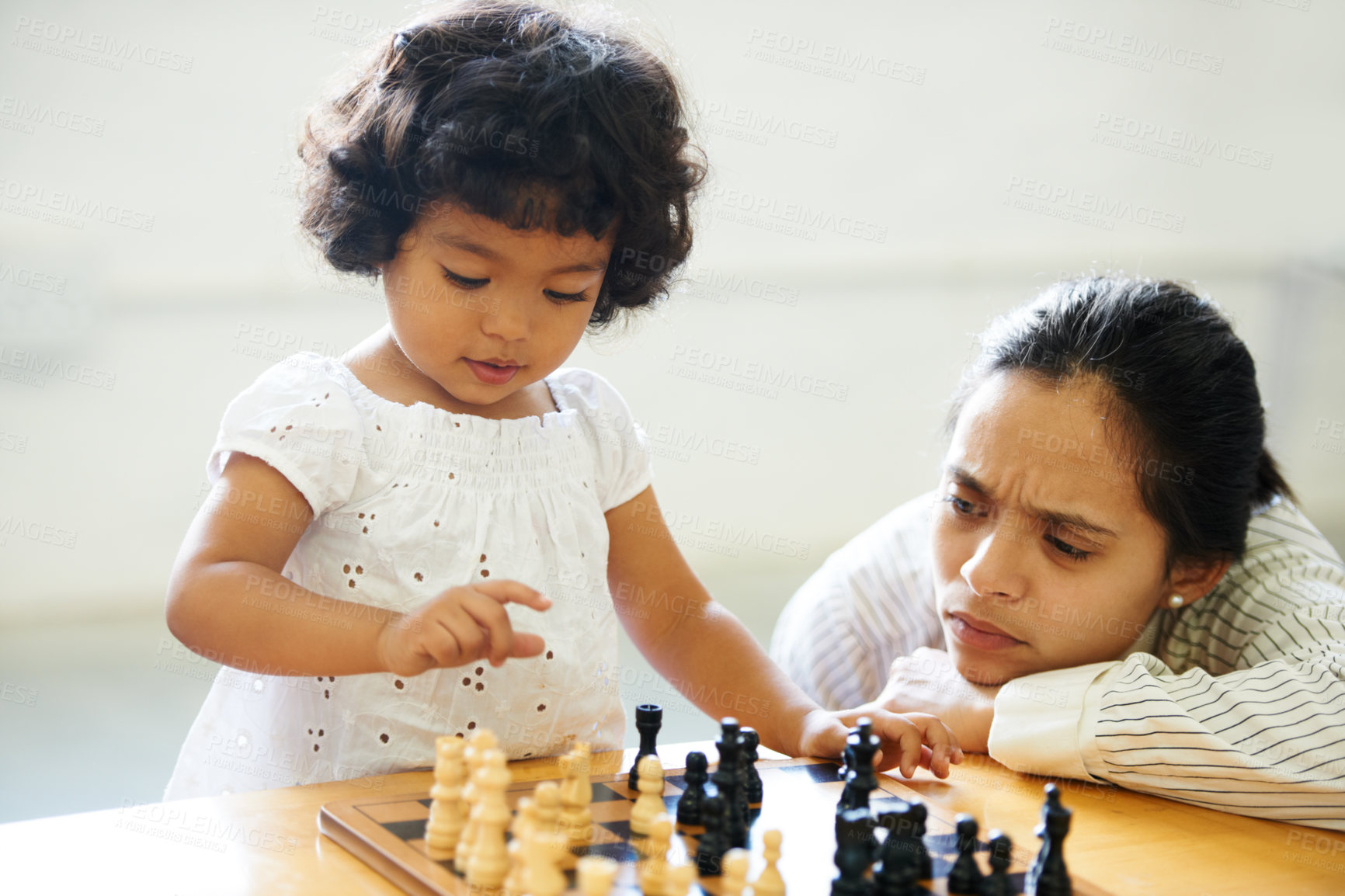 Buy stock photo A cute little girl playing chess while her mom looks on