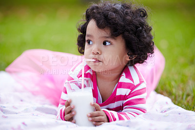 Buy stock photo Adorable little girl drinking milk through a straw while lying on the grass