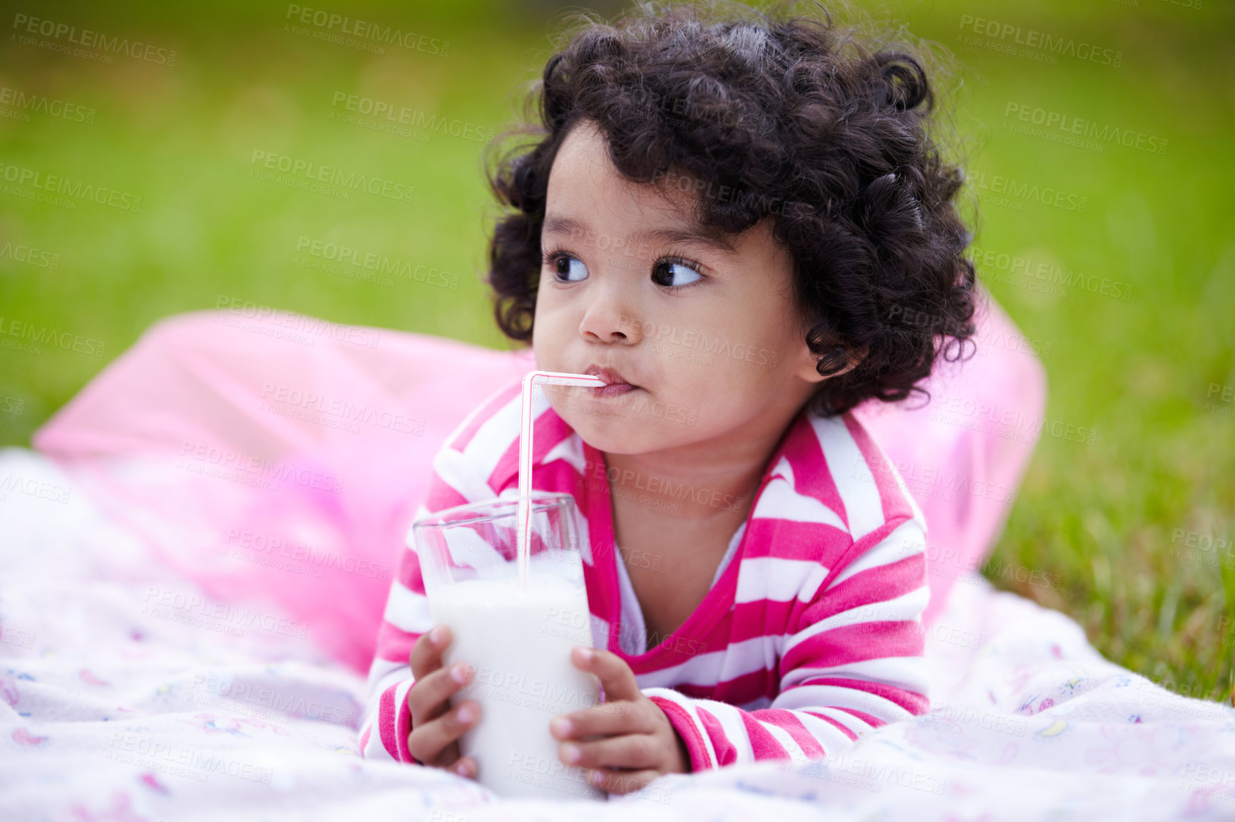 Buy stock photo Adorable little girl drinking milk through a straw while lying on the grass