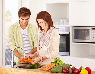 Buy stock photo A happy couple washing some carrots in the kitchen sink