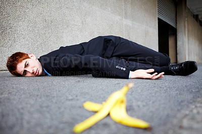Buy stock photo A young man lying on the ground after slipping on a banana peel