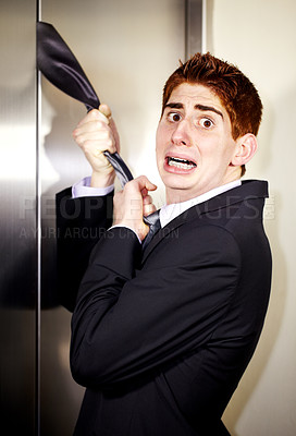 Buy stock photo A young businessman with his tie stuck in the elevator