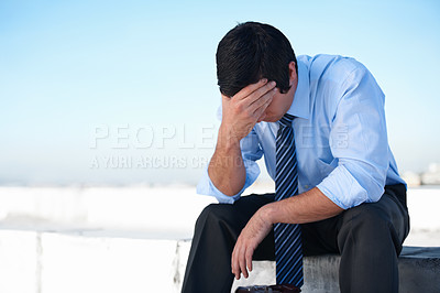 Buy stock photo An upset corporate man sitting on the rooftop of a building with his head in his hands