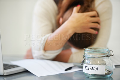 Buy stock photo An upset woman holding her head with a jar of pennies on her desk