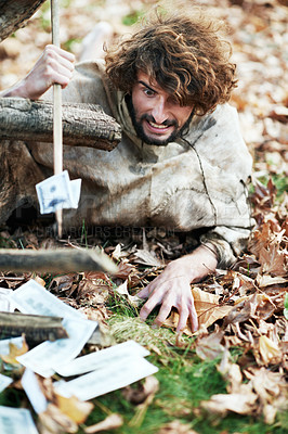 Buy stock photo A crazy looking caveman crawling on the ground and piercing money with his spear