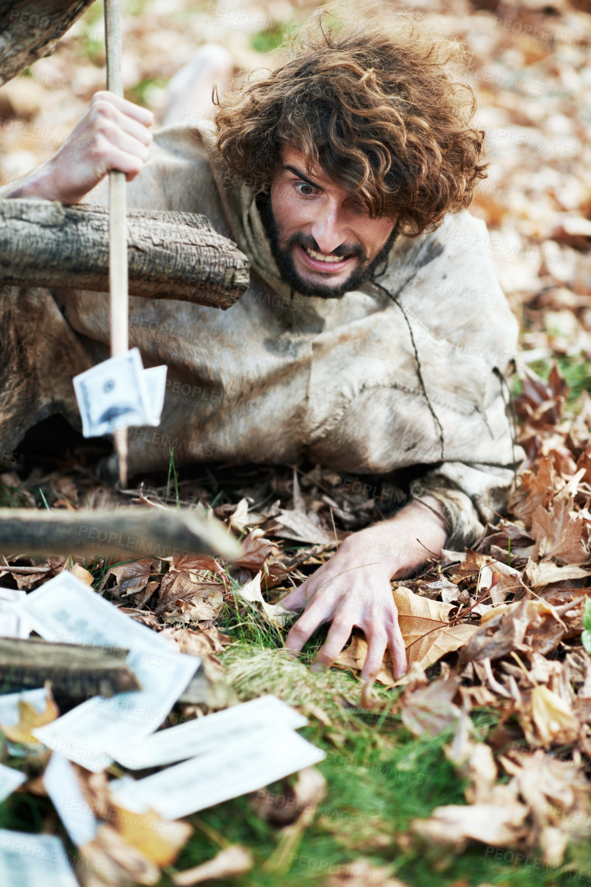 Buy stock photo A crazy looking caveman crawling on the ground and piercing money with his spear