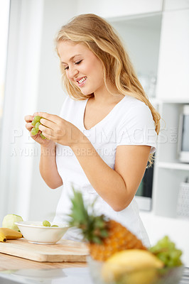 Buy stock photo Curvaceous young woman eating grapes in her kitchen