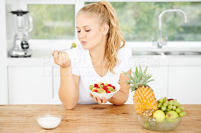 Buy stock photo Attractive young woman eating fruit salad in her kitchen