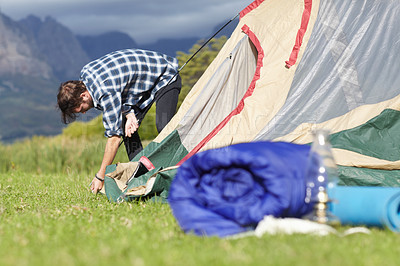 Buy stock photo Nature, camping and man building a tent in countryside with mountain, environment and grass. Adventure, shelter and person start with pitching equipment to ground for secure outdoor camper structure
