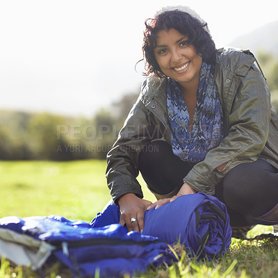 Buy stock photo Attractive young woman unrolling a sleeping bag on the grass