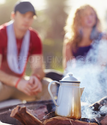 Buy stock photo Coffee brewing on an outdoor camp fire with a young couple in the background