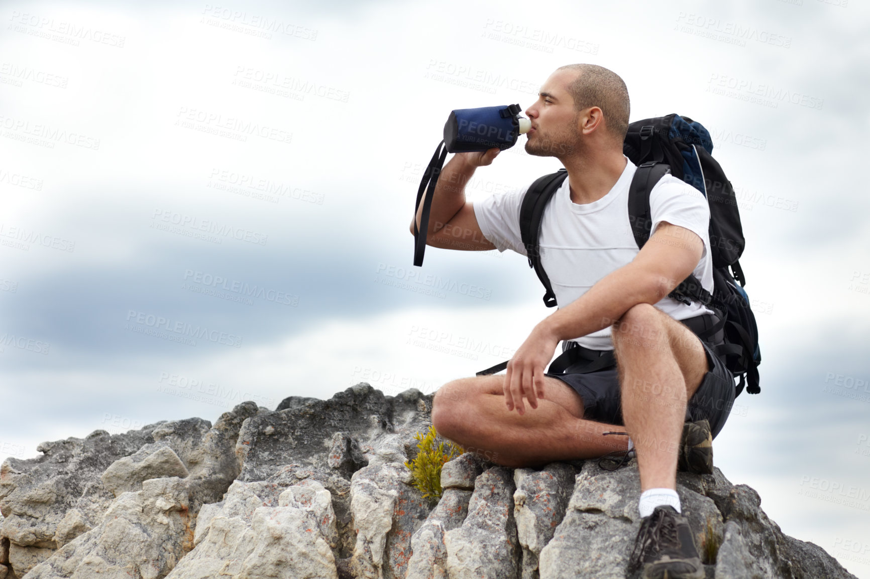 Buy stock photo A young man taking a break from hiking while sitting on a rock and drinking some water
