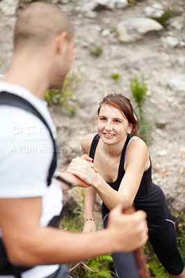 Buy stock photo A young man helping his girlfriend upa rock while on their hike