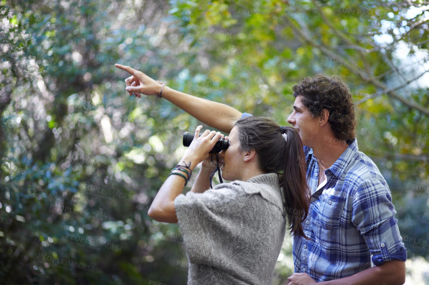 Buy stock photo A young man pointing something out to his girlfriend while she looks through binoculars