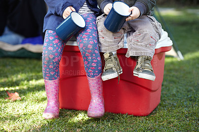 Buy stock photo Closeup of two two kids holding mugs and sitting on a cooler box in a park with copyspace. Hungry children waiting for breakfast while out camping. Brother and sister enjoying a warm drink together