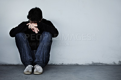 Buy stock photo A young man looking sad while sitting on the ground with his head on his hands