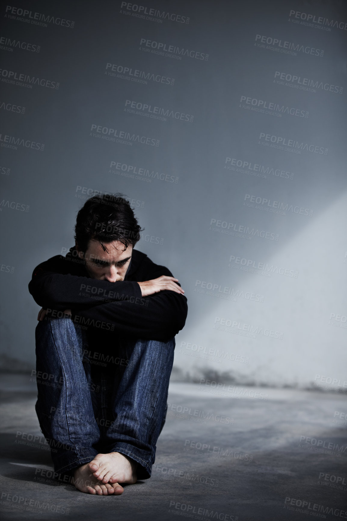 Buy stock photo A young man looking worried while sitting barefoot on the ground