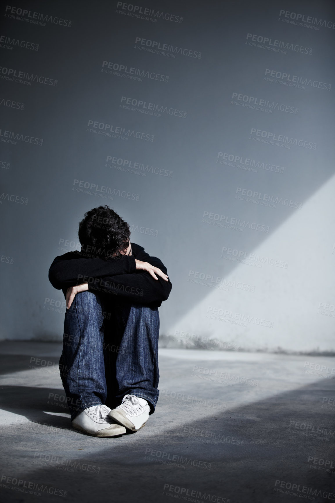 Buy stock photo A young man sitting on the ground and resting his head on his folded arms