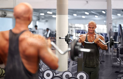 Buy stock photo Shot of a male bodybuilder looking in the mirror while lifting weights at the gym