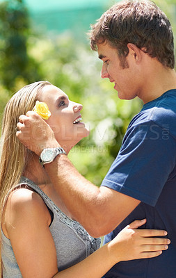Buy stock photo A young man placing a flower over his girlfriend's ear while looking lovingly at her