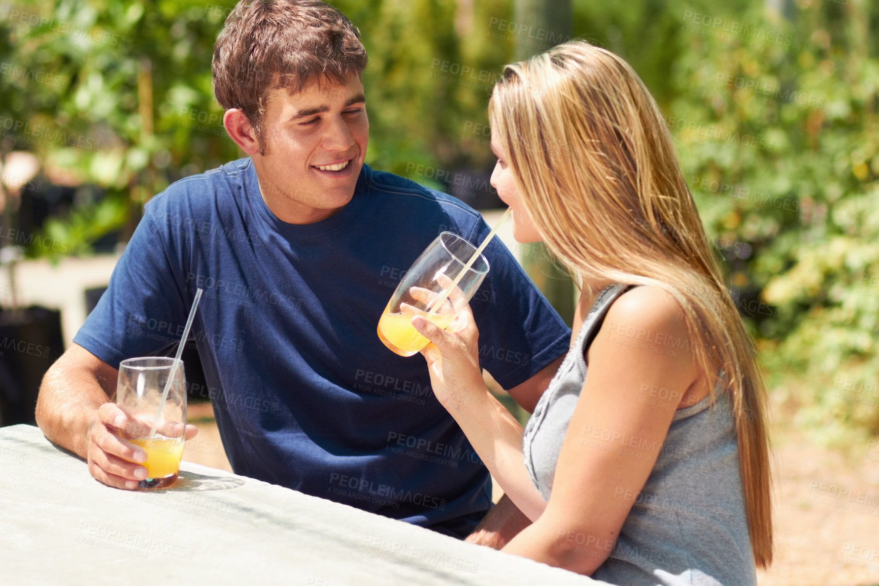 Buy stock photo A young couple sitting outside and drinking orange juice