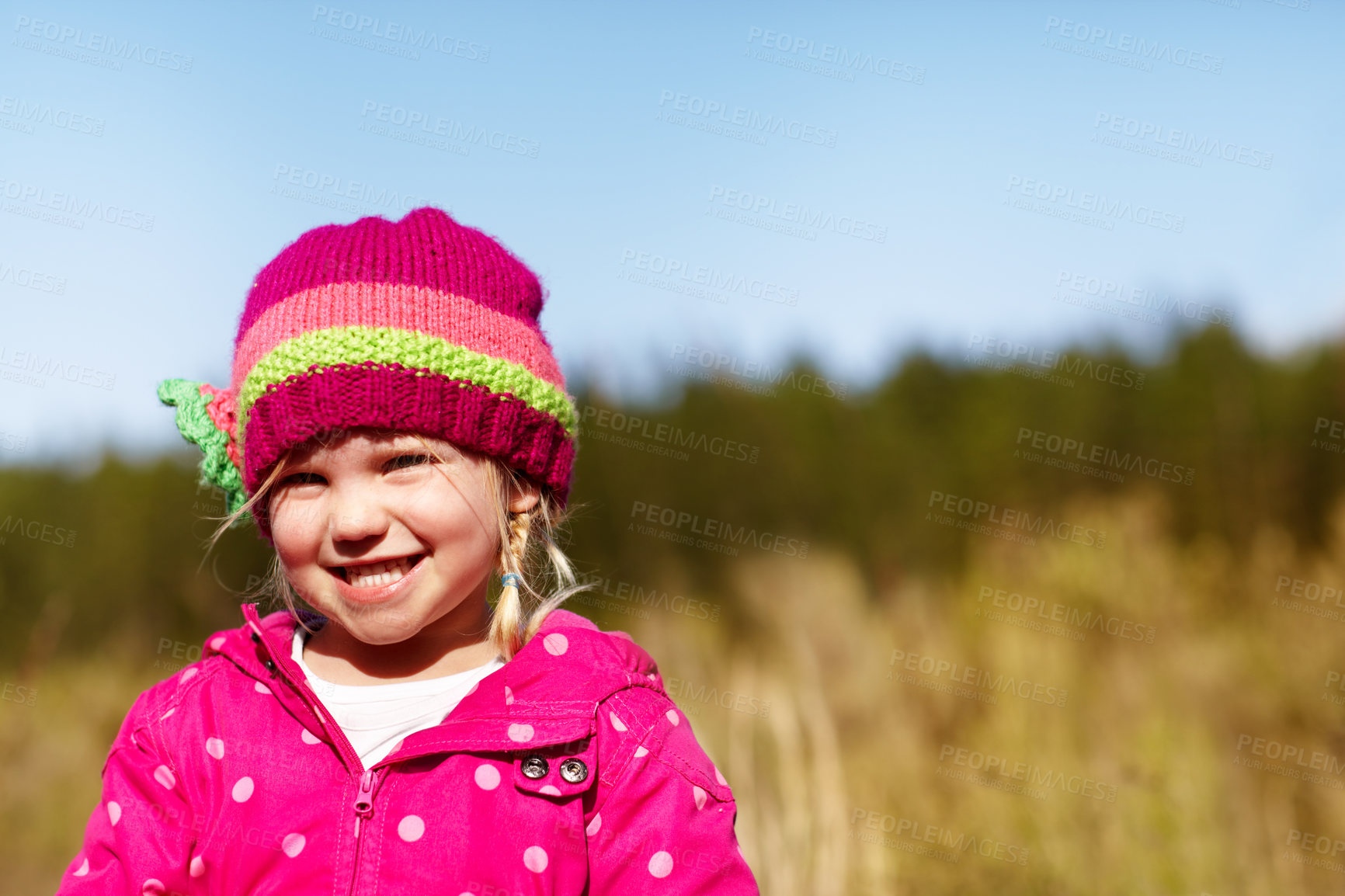 Buy stock photo Portrait of a cute little girl smiling looking happy dressed warm and wearing a pink hat outdoors in nature on a cold autumn day. Adorable young female looking joyful while playing outside in a field