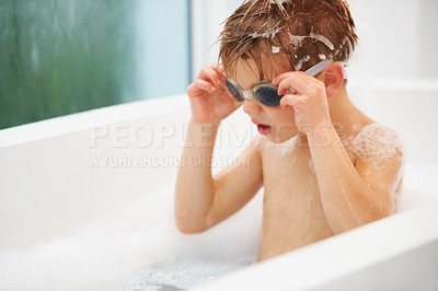 Buy stock photo Kids, bath and a boy in swimming goggles having fun while cleaning for hygiene in water. Soap, wellness and bubbles with a curious young child alone in the bathroom to wash for fresh skincare