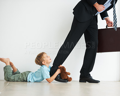 Buy stock photo A young boy holding onto his dad's leg to try and stop him from leaving to work